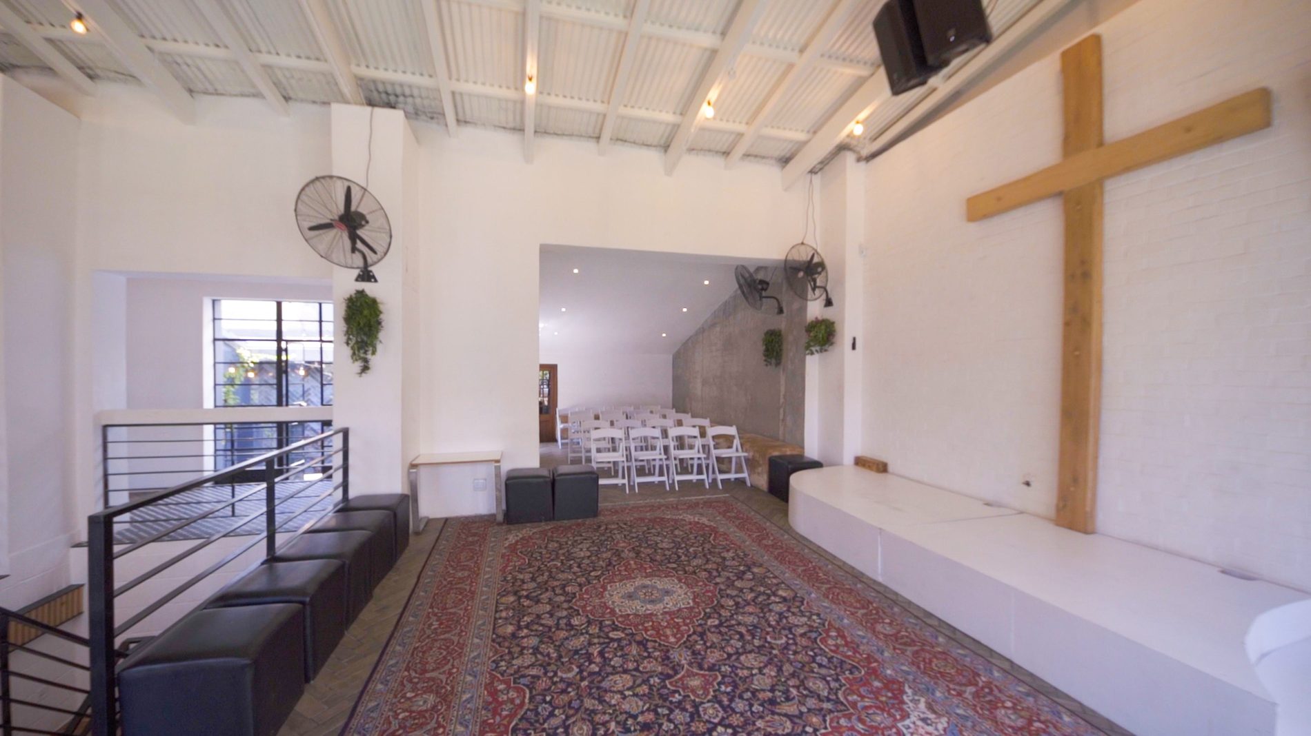The main hall at The Well, set with white chairs beneath a wooden cross